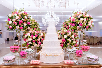 a golden wooden table, with a wedding cake in the center, decorated with vases of rose flowers and sweets
