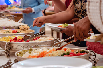 a table with a buffet served on silver platters and hands serving the food - Powered by Adobe
