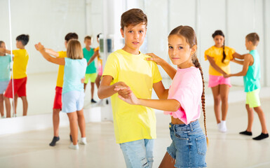 Interested modern tween boy and girl practicing slow pair dancing during group class in dance...
