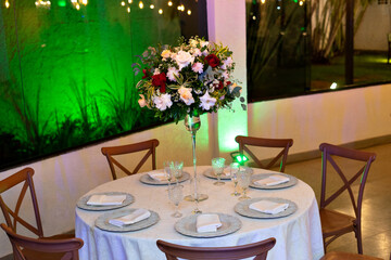 a glass dining table decorated with plates and flowers, with wooden chairs around it