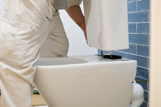 Unrecognizable senior plumber installer installing toilet cistern in a bathroom.