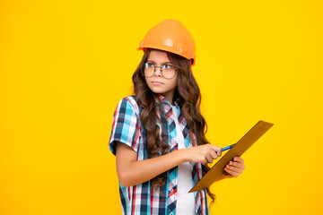 Thinking pensive clever teenager girl. Teenager child painter in helmet with clipboard. Child in hard hat. Kid engineer on construction site. Renovation and repair. - obrazy, fototapety, plakaty