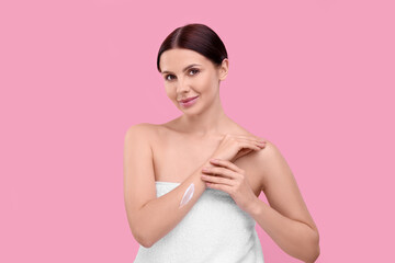 Beautiful woman with smear of body cream on her arm against pink background