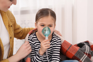 Mother covering her daughter with plaid while she using nebulizer for inhalation at home