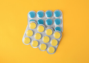 Blisters with cough drops on yellow background, flat lay