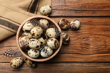 Obraz na płótnie Canvas Speckled quail eggs and feathers on wooden table, flat lay. Space for text
