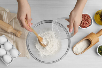 Woman putting flour into bowl at wooden table, top view