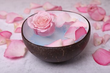 Beautiful composition with bowl of water and rose petals on light table, closeup. Spa treatment