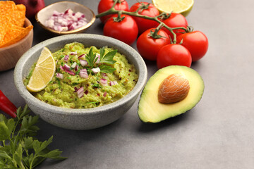 Bowl of delicious guacamole, nachos chips and ingredients on grey table, closeup. Space for text