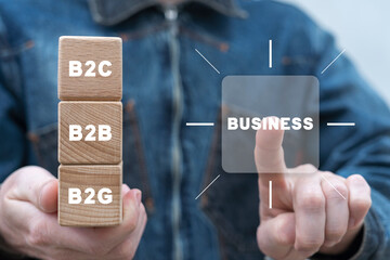 Man using virtual touchscreen clicks BUSINESS word and holding wooden cubes with abbreviation: B2C, B2B, B2G. Concept of business marketing process. Business to business, to customer and to government