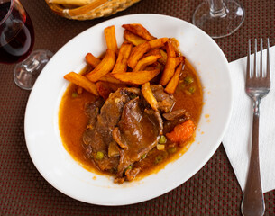 Appetizing braised beef meat in thick spicy vegetable gravy served with side dish of crispy fried potatoes