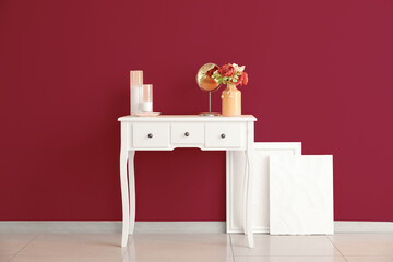 Vase with flowers, mirror and candles on table near pink wall