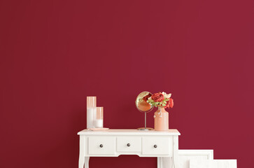 Vase with flowers, mirror and candles on table near pink wall