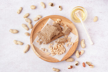 Fototapeta na wymiar Wooden plate with pieces of tasty halva and peanuts on white background