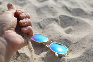 The hand pours out sand in front of the glasses lying on the sand
