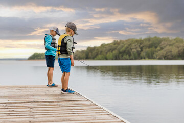 Two young boys fishing on a dock at dusk wearing life jackets