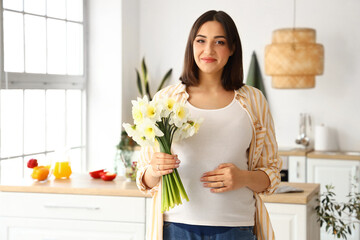 Fototapeta na wymiar Young pregnant woman with narcissus flowers in kitchen