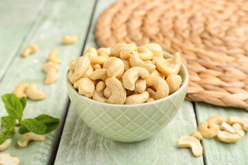 Bowl with tasty cashew nuts on light wooden background