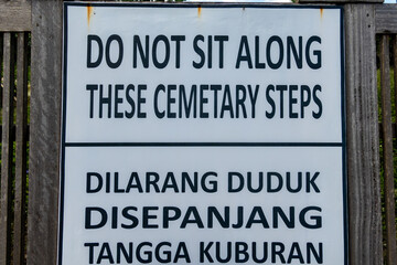 Canggu, Bali, Indonesia, A sign on the beach in English and Indonesian says not to sit on cemetery steps.