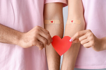 Young couple after donating blood with paper heart on light background