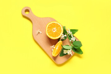 Wooden board of oranges with blooming branch on yellow background