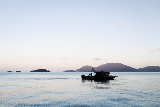 Small Fishing Boat on Calm Sea at Sunrise with Distant Islands