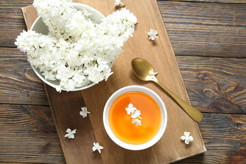 Board with beautiful lilac flowers and cup of tea on wooden background