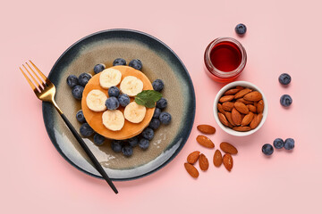 Plate with sweet pancakes, nuts and honey on pink background