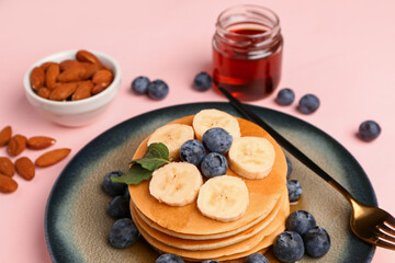 Plate with sweet pancakes, nuts and honey on pink background, closeup