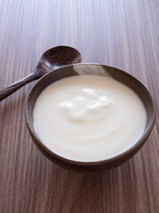 Fototapeta na wymiar Homemade greek yogurt or sour cream in old clay bowl with wooden spoon on wooden background. Food helps the digestive system..