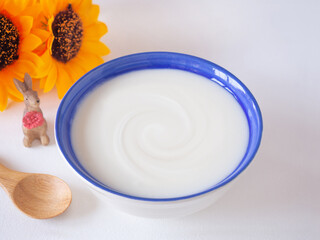 Homemade greek yogurt or sour cream in blue bowl with wooden spoon, and yellow flower over white wooden background. Food helps the digestive system..