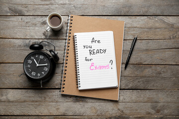 Notebooks with question ARE YOU READY FOR EXAM?, cup of coffee and alarm clock on brown wooden background