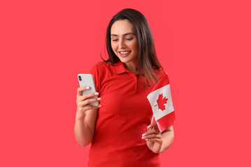 Young woman with flag of Canada using mobile phone on red background