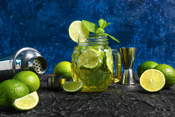 Mason jar of cold mojito and shaker with lime on black table
