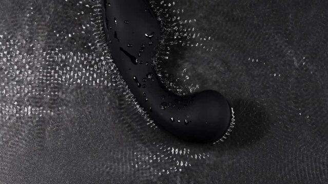 The black prostate stimulator vibrates and creates ripples on the surface of the water against a black background.