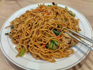 Close up view of stir fry noodles with vegetables and shrimps in white plate. Spicy stir fried noodle with chopsticks.
