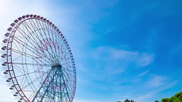 A timelapse of moving ferris wheel at the park behind the blue sky wide shot panning