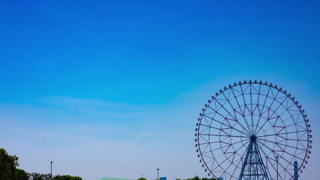 A timelapse of moving ferris wheel at the park behind the blue sky wide shot panning