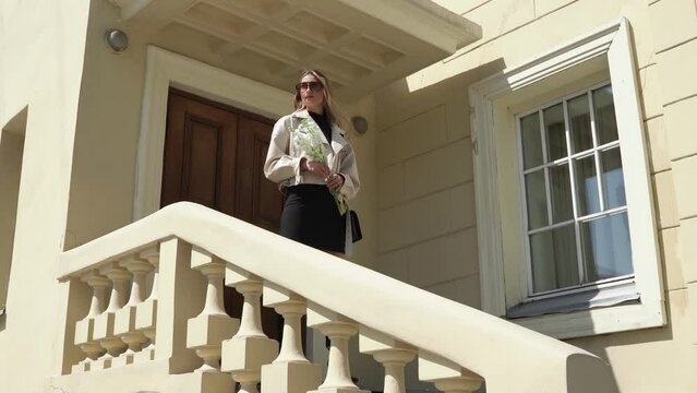young woman with flowers in white jacket on the staircase outdoors