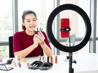 Asian makeup artist woman review how to use brush set tutorial and record live video for sharing with smartphone and selfie circle ring light in the studio designer room