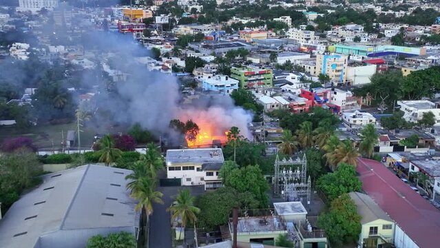 Drone shot approaching a flaming and smoking house in middle of a tropical city
