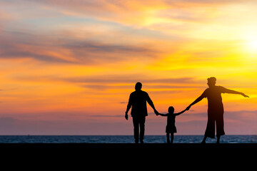 Fototapeta na wymiar Silhouette of Family holding hands enjoying with sunset on the beach, Mom dad and daughter playing on the beach