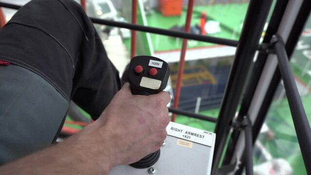 Hand takes joystick and pull. Inside crane cabin. Crane operator works