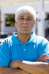 Portrait of senior biracial man looking at camera with arms crossed in sunny garden