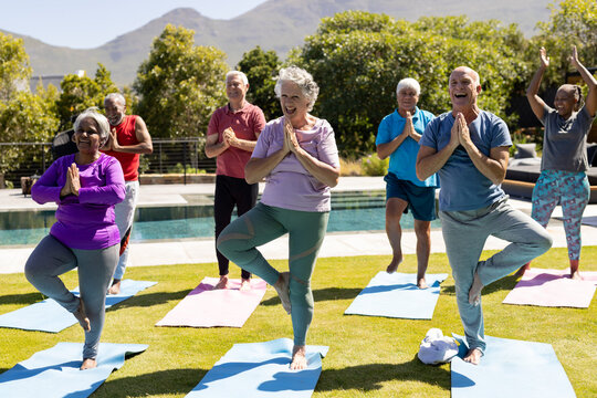 Happy diverse senior friends practicing yoga standing in sunny garden
