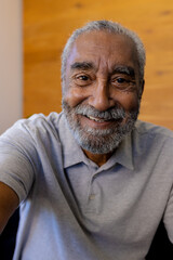 Happy senior biracial man with beard making video call sitting and smiling at home