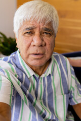 Senior biracial man in striped shirt making video call sitting at home