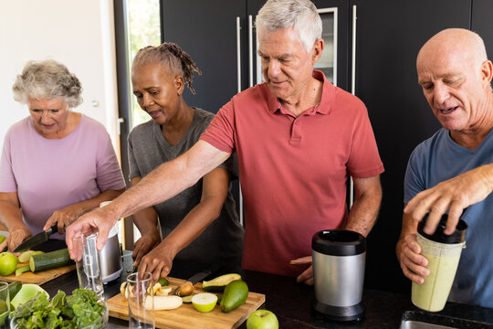 Happy diverse senior friends talking and preparing healthy smoothies together in kitchen