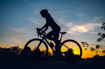 Fototapeta premium Silhouette of a woman riding a bike during a sport cycling race on a sunset