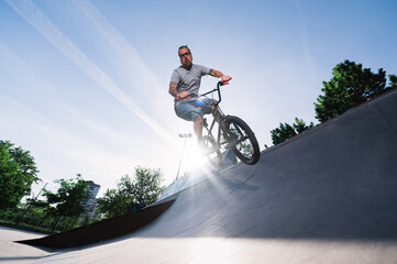 A professional middle-aged bike rider is jumping with his bmx bike on a ramp in a skate park.